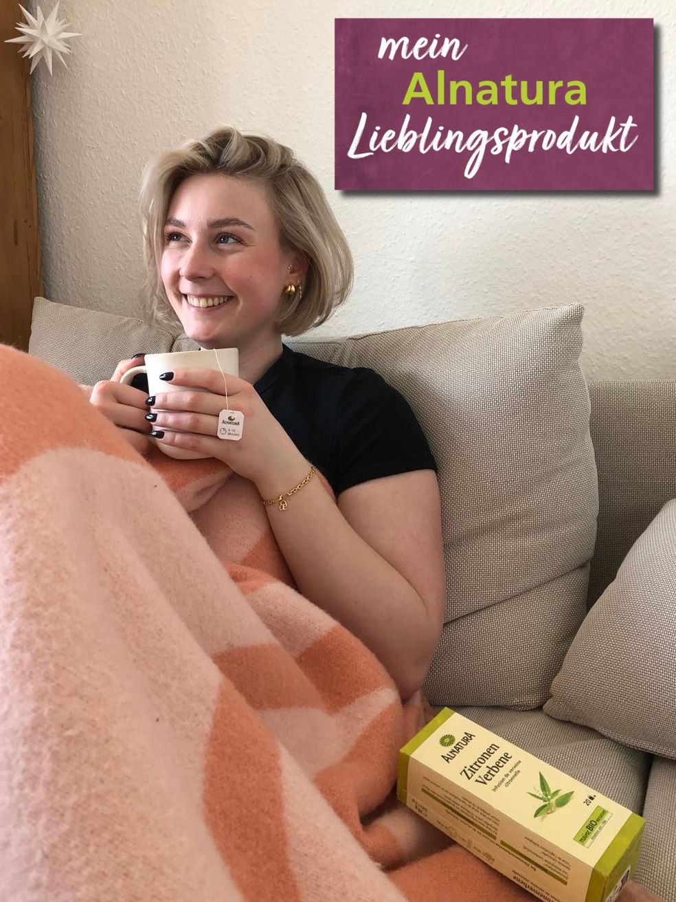 Alnatura Kundin Lea liegt mit einer Tasse Tee und einer Decke auf dem Sofa. Neben ihr liegt ihr Alnatura Lieblingsprodukt, der Zitronenverbenentee.