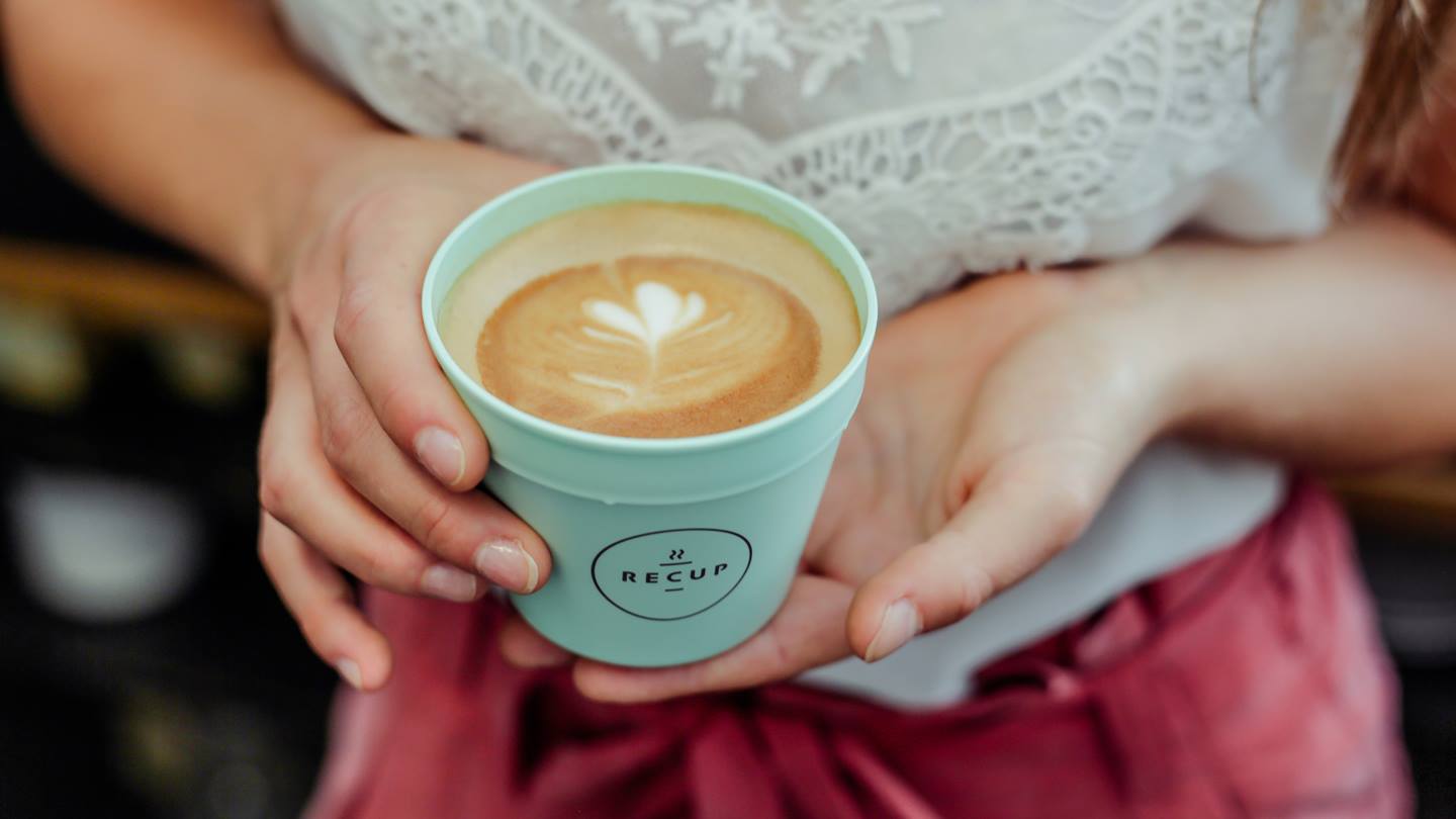 Recup-Pfandbecher mit Cappuccino gefüllt und gehalten von einer Frau