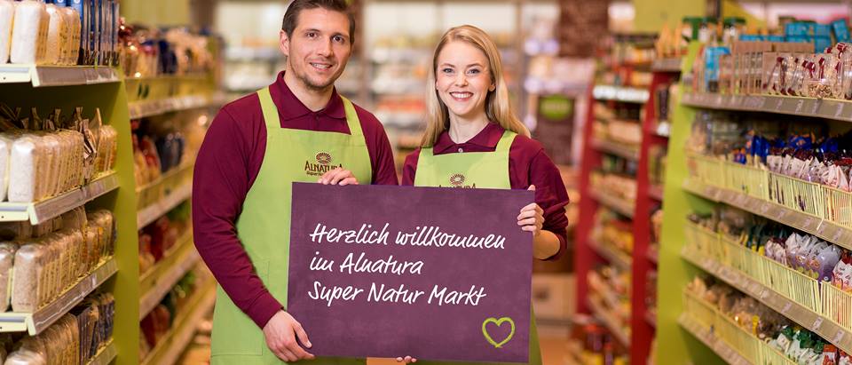 Zwei Mitarbeitende wünschen Herzlich Willkommen im Alnatura Super Natur Markt