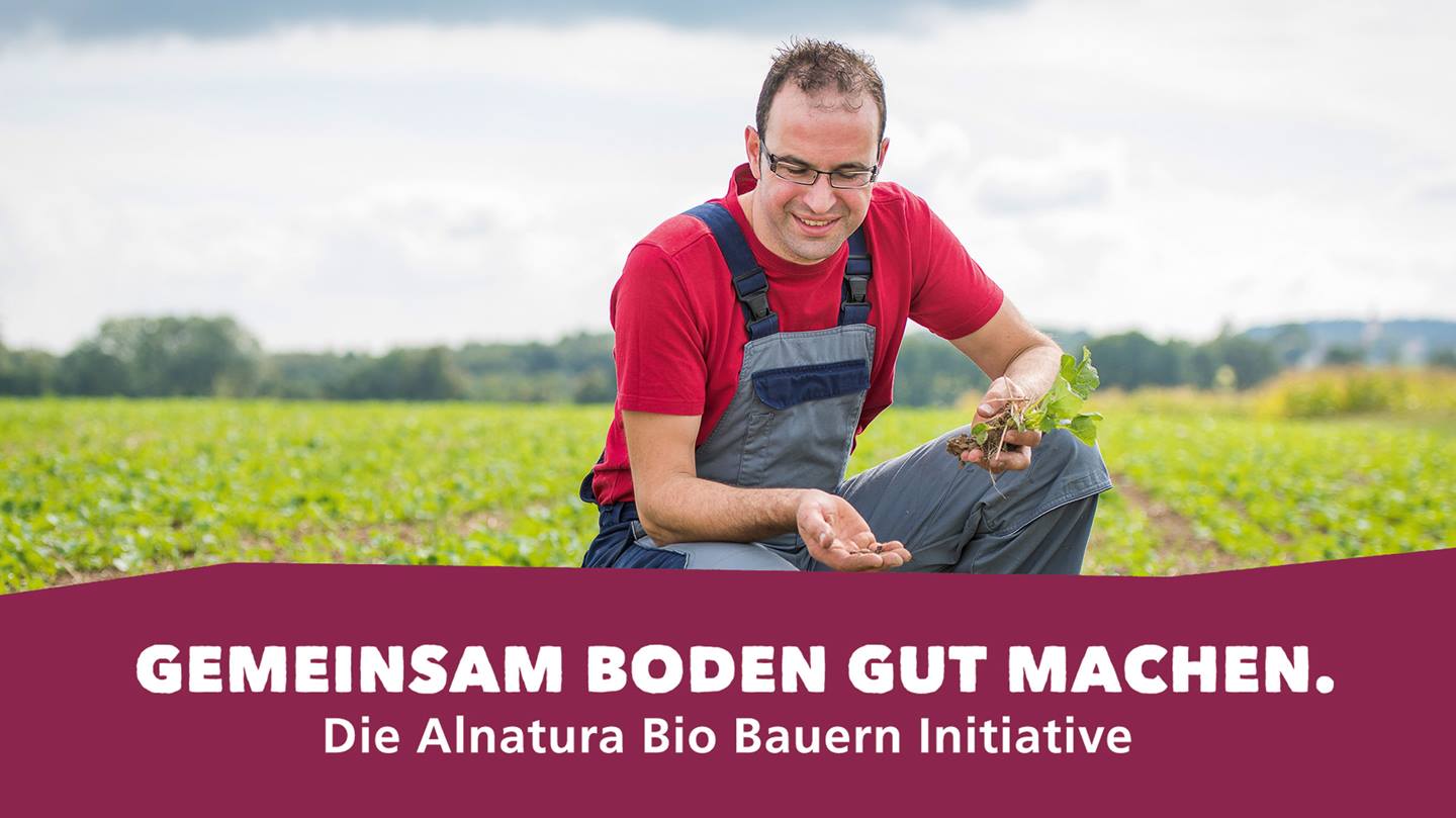 Bio-Bauer auf Feld mit Logo der Alnatura Bio-Bauern-Initiative