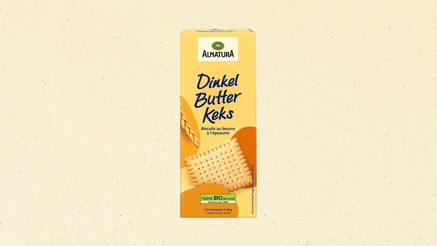 Das Bild zeigt eine Verpackung von Alnatura Dinkel Butter Keksen. Die Verpackung ist gelblich und zeigt ein Bild eines Butterkekses. Der Markenname Alnatura ist prominent platziert, ebenso wie die Produktbezeichnung "Dinkel Butter Keks" in blauer Schrift. Zusätzliche Informationen wie die Zutaten (Biscuits au beurre à l'épeautre) und die Packungsgröße (3 x 50g) sind ebenfalls auf der Packung zu finden. Das Gesamtbild wirkt sauber und appetitlich.