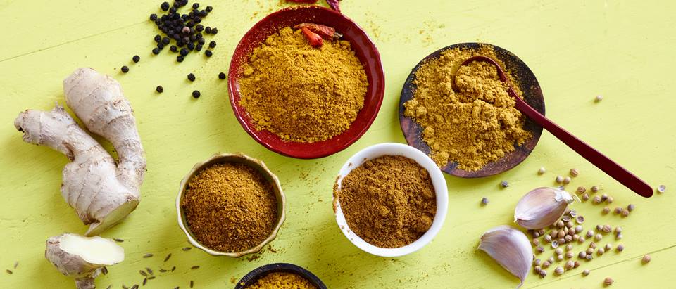 verschiedene Currypulver Sorten in Schälchen, Knoblauchzehen, schwarze Pfefferkörner, bunte Pfefferkörner
