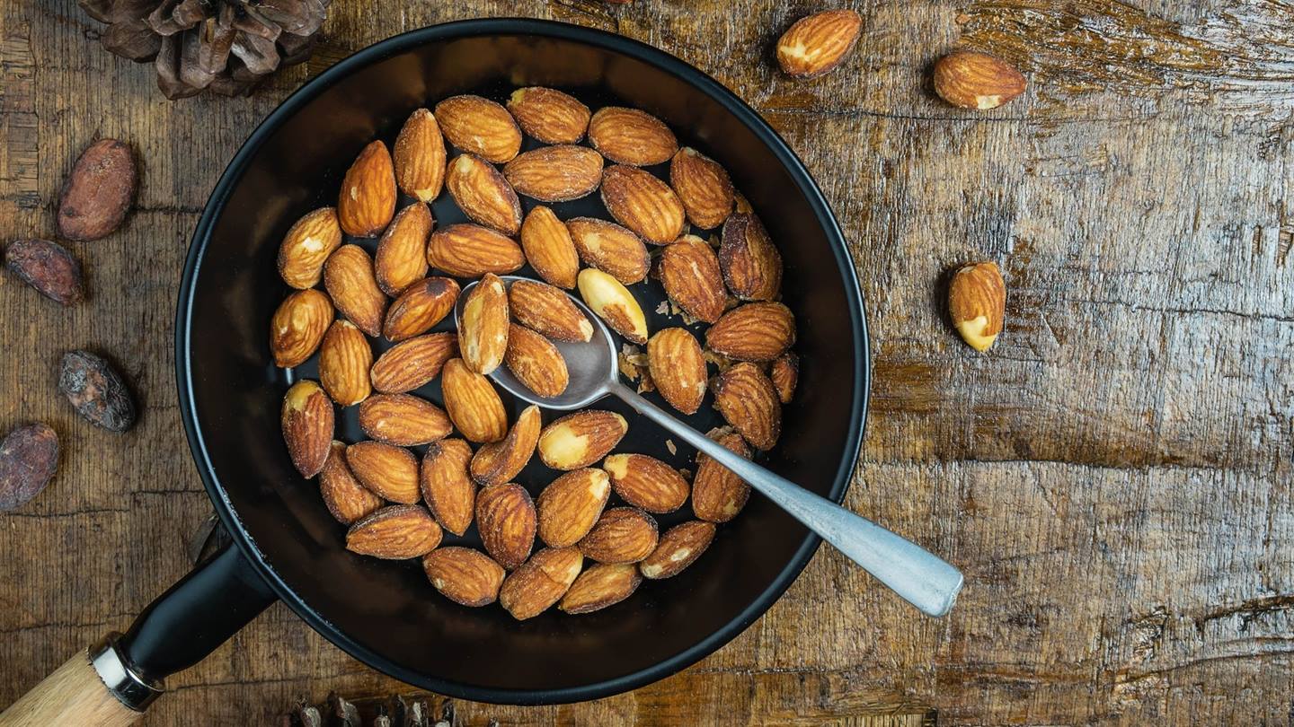geröstete Mandeln in einer Pfanne auf einem Holztisch mit einem Löffel
