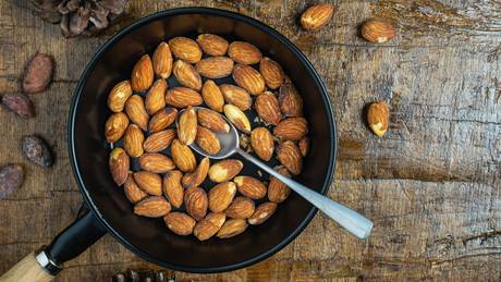 geröstete Mandeln in einer Pfanne auf einem Holztisch mit einem Löffel