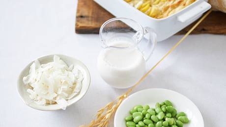 Vegane Sahnealternative in kleinem Glaskrug und Schalen mit Kokosflocken und Sojabohnen