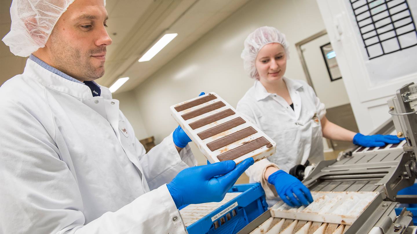 Der Produktionsleiter Tijs Roeland hält eine Form mit Lovechock Riegeln in der Hand, im Hintergrund eine weitere Mitarbeiterin