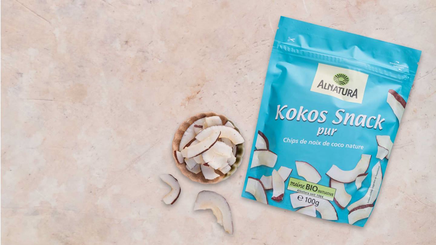 Eine Packung Alnatura Kokos Snack Pur liegt neben einer Schale mit Kokoschips.