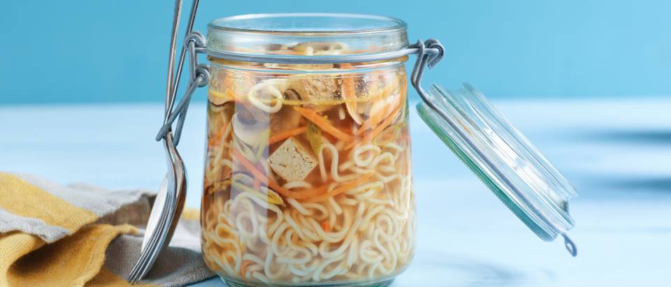 Alnatura Rezept: Ein Glas mit Instant Nudelsuppe mit einem Esslöffel auf einem Tisch.
