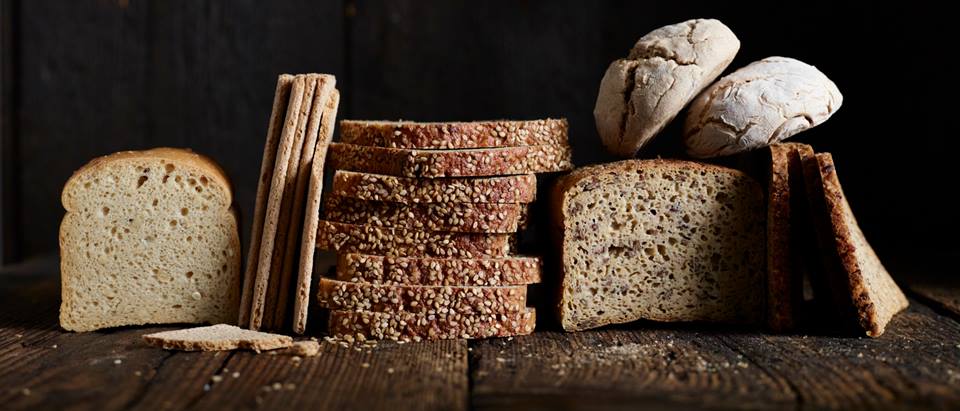 Verschiedene Sorten Brot aufgestapelt sowie aufgeschnittene Brote nebeneinander vor einem schwarzem Hintergrund. Es soll zum Brot selber backen inspirieren.