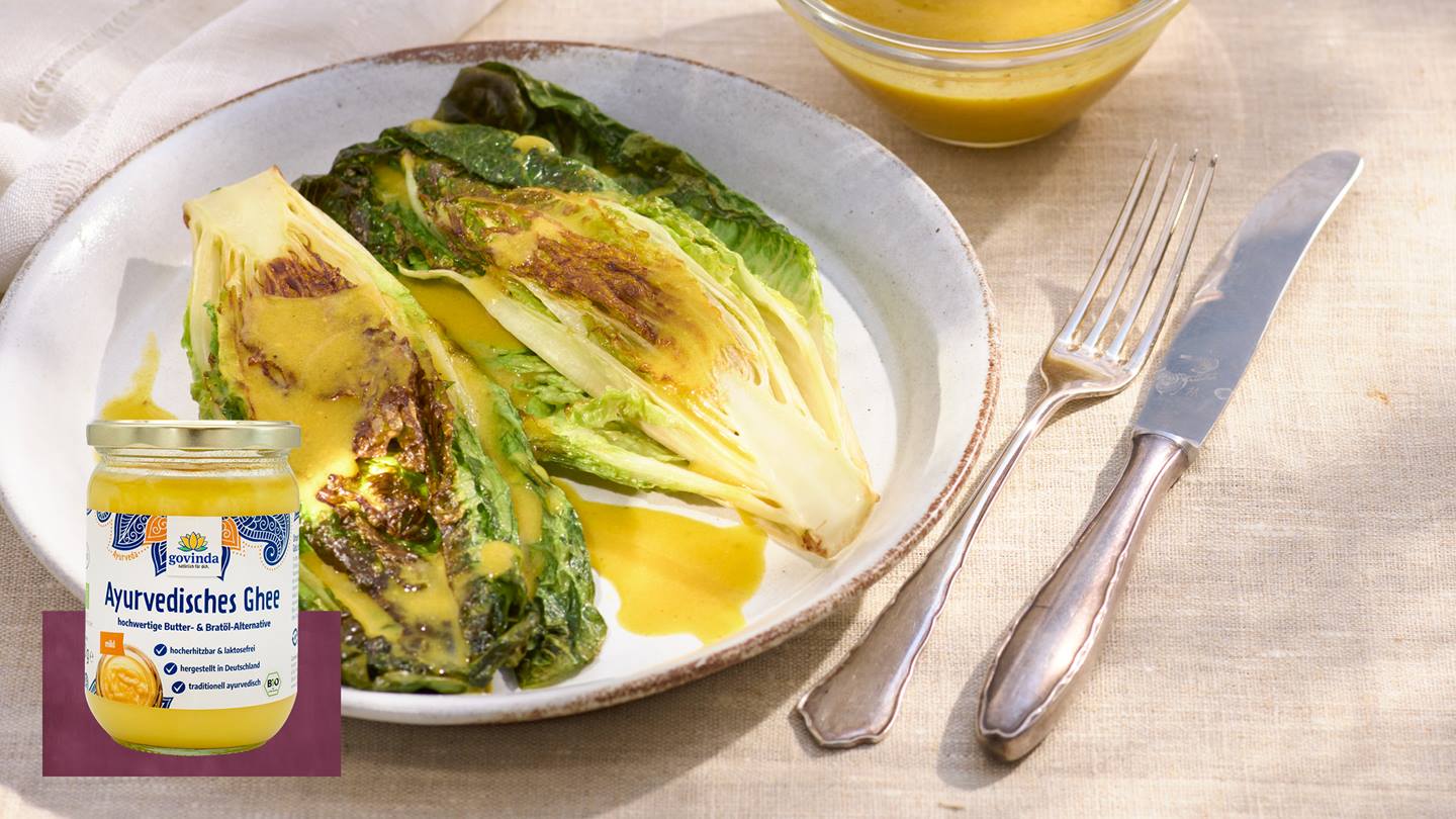 Teller mit gebratenem Romana-Salat und etwas Soße darauf. Im Vordergrund ein Glas Ayurvedisches Ghee der Marke Govinda.