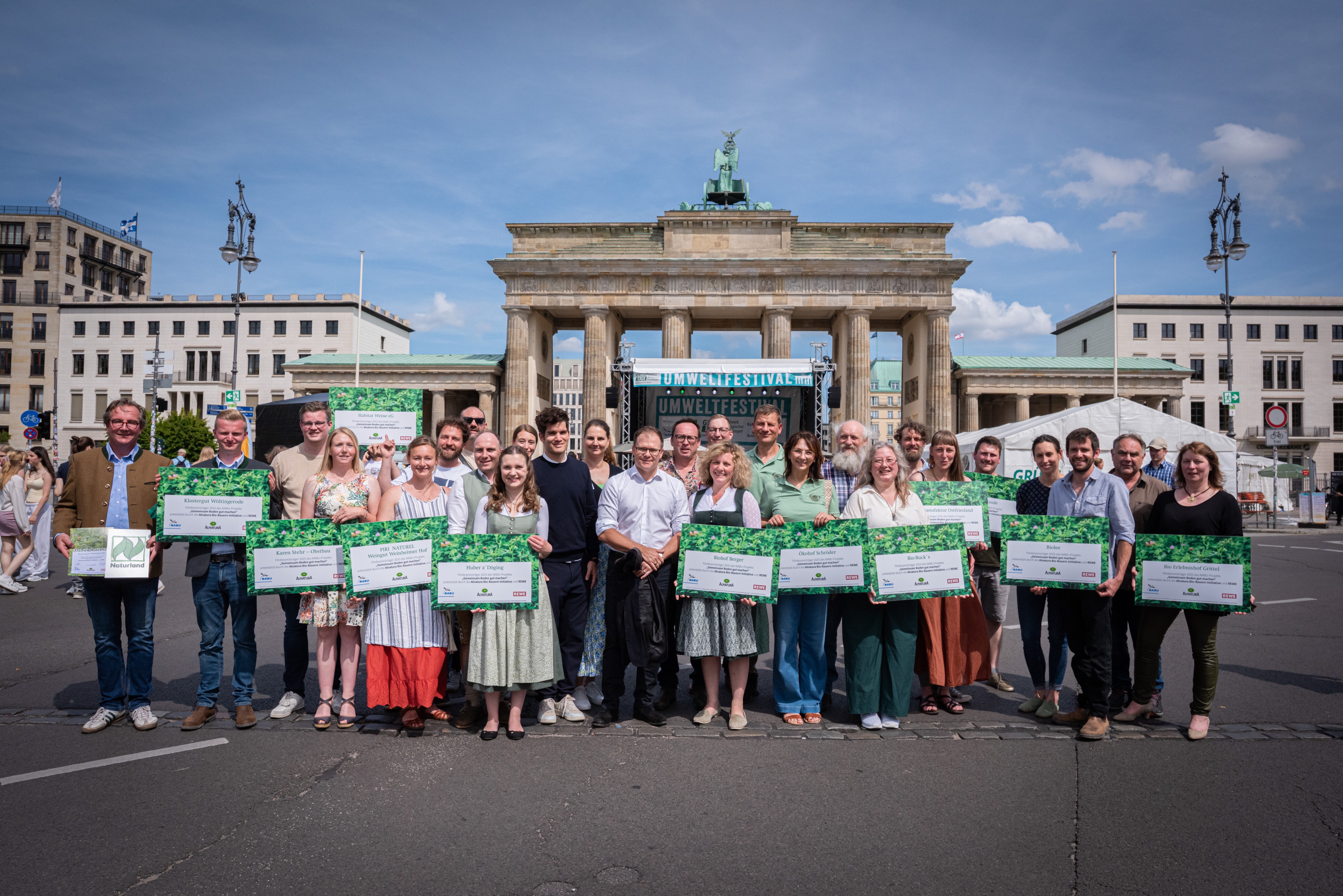 Gruppe von Menschen steht vor dem Brandenburger Tor und hält große grüne Schilder mit Text.