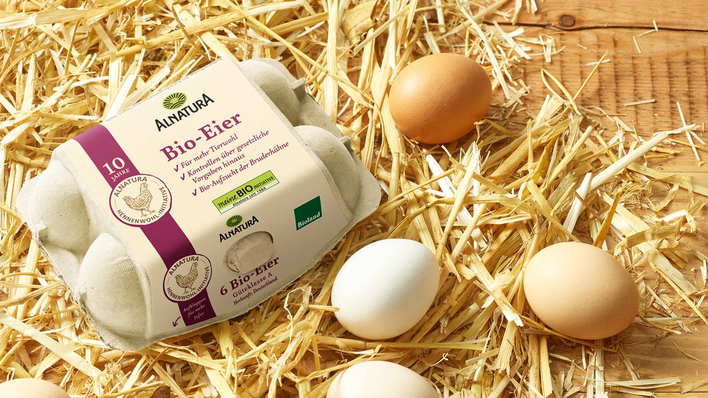 Alnatura Bio-Eierpackung und lose Eier auf Heu liegend