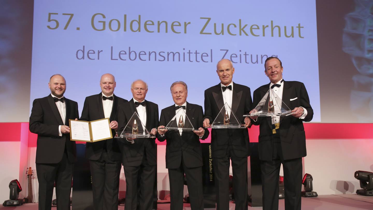 Sechs Herren im Anzug stehen auf einer Bühne anlässlich der Verleihung des 57. Goldener Zuckerhut der Lebensmittel Zeitung. Einer der Herren ist Prof. Dr. Götz Rehn, der Gründer und Inhaber von Alnatura. Alle halten Ihren Auszeichnungen in Händen..