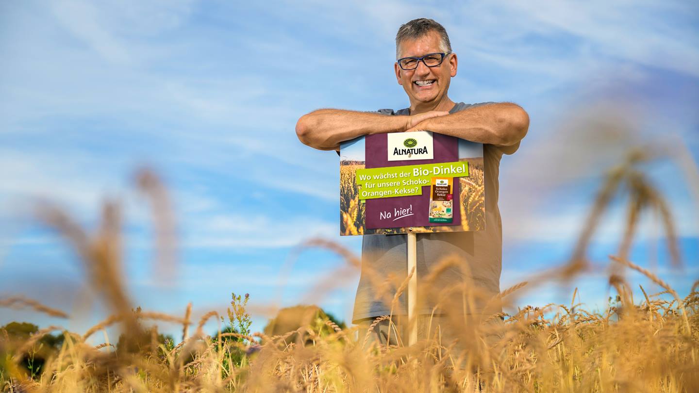 Klaus Laub in seinem Dinkelfeld mit Schild für die Alnatura Schoko-Orangen-Kekse