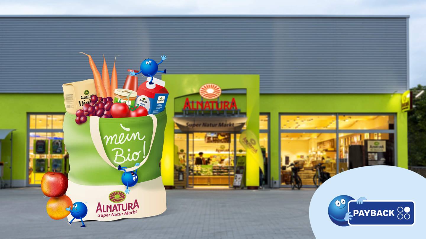 Das Bild zeigt eine grüne Einkaufstasche voller Bio-Lebensmittel vor einem Alnatura Super Natur Markt. Die Tasche ist mit dem Slogan „mein Bio!“ beschriftet und zeigt das Alnatura-Logo. Kleine, animierte blaue Figuren interagieren mit der Tasche und den Lebensmitteln. Im Vordergrund ist ein PAYBACK-Logo zu sehen, das auf ein Treueprogramm hindeutet. Das Gesamtbild ist Werbung für Bio-Produkte und den Alnatura-Markt mit dem verbundenen Partnerprogramm PAYBACK.