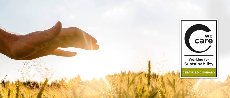 Hand im Vordergrund über einem Getreidefeld, mit We-Care-Siegel im Vordergrund