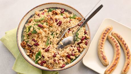 Schüssel mit Quinoasalat aus Quinoa, Kidneybohnen, Kichererbsen, Walnüssen und grünen Blättern neben Teller mit drei gegrillten Bratwürsten.