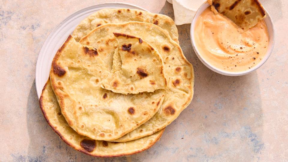 Drei runde Dinkelfladenbrote auf weißem Teller neben Schale mit cremigem Dip.