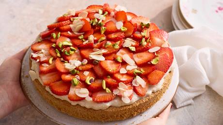Erdbeerkuchen mit Sahne, Mandelsplittern und Pistazienstückchen auf einem Teller, gehalten von zwei Händen.