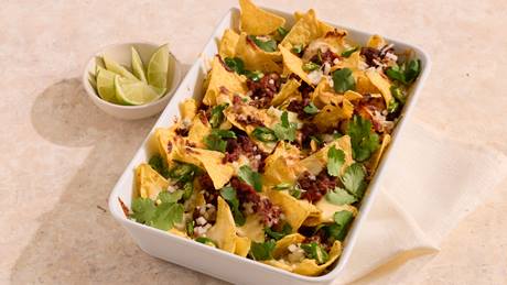 Auflaufform mit Chili-Cheese-Nachos, garniert mit Koriander und Limettenspalten daneben.