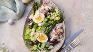 Ein Teller mit Salat nicoise und Besteck stehen auf einem grauen Untergrund 