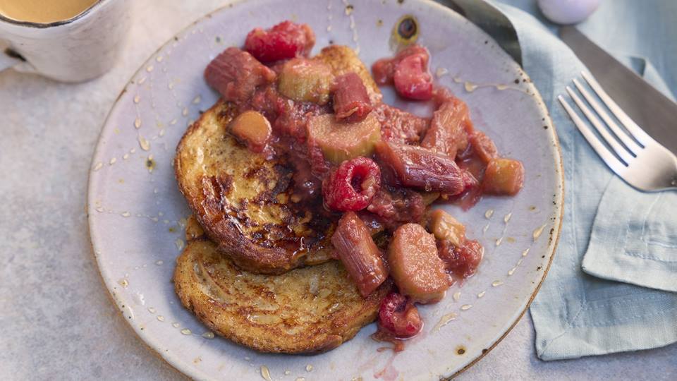 Auf einem Teller sind zwei French Toast garniert mit pochiertem Rhabarber. Eine Gabel und eine Stoffserviette sind rechts im Anschnitt zu sehen.