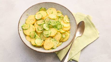 Schale mit Kartoffel-Gurkensalat und Löffel auf grünem Stoffserviette.
