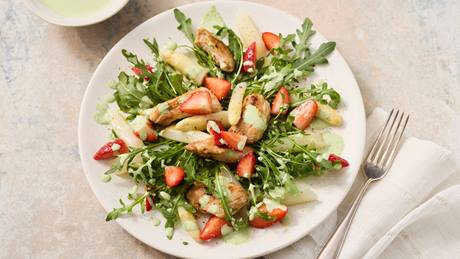 Teller mit Salat aus weißem Spargel, Erdbeeren, Rucola und Hähnchenstreifen, daneben eine Gabel auf weißem Stoffserviette.