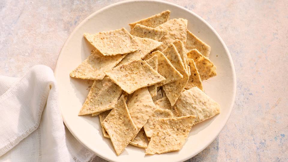 Weißer Teller mit rechteckigen Sesam-Crackern auf hellem Untergrund neben weißem Stoffserviette.