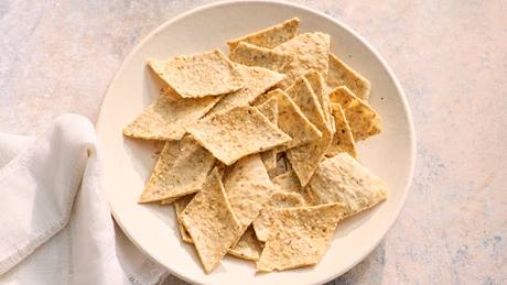 Weißer Teller mit rechteckigen Sesam-Crackern auf hellem Untergrund neben weißem Stoffserviette.