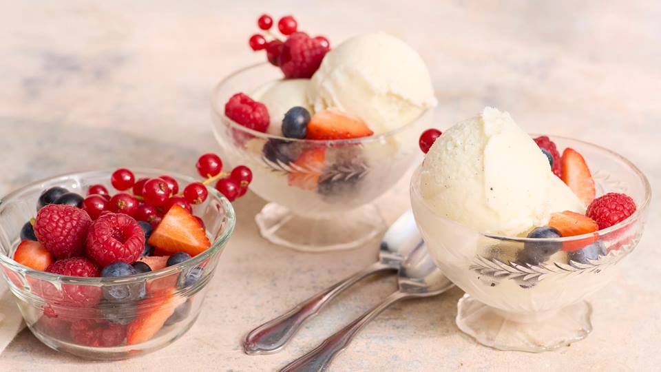 Drei Glasschalen mit je einer Kugel Frozen Yogurt und frischen Beeren wie Himbeeren, Erdbeeren, Heidelbeeren und roten Johannisbeeren auf hellem Untergrund.