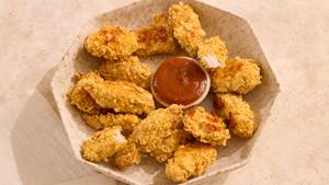 Schale mit panierten Chicken Nuggets und einer kleinen Schale mit roter Sauce in der Mitte.
