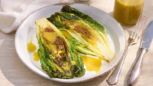 Gegrillter Duo Bratsalat und Honig Senf Dressing auf weißem Teller mit mehr Honig Senf Dressing in Glasschale dahinter und Besteck auf hellem Untergrund.