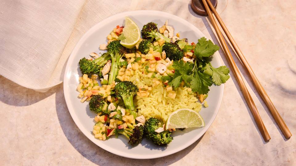 Kokos-Curry-Reis mit Brokkoli und Limettenscheiben auf hellem Teller, mit Stäbchen und beige Serviette.