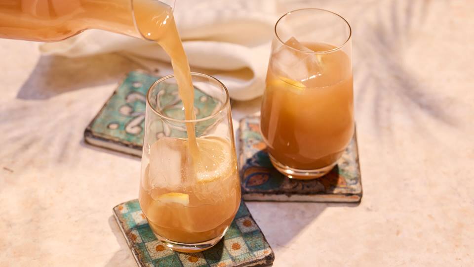 Zwei Gläser mit Pfirsich-Eistee, während Pfirsichsaft aus Karaffe eingeschenkt wird, Servietten im Hintergrund