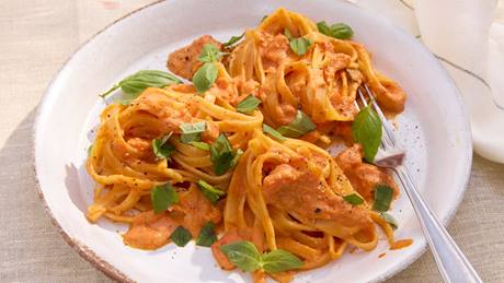 Drei Portionen Pasta mit cremiger Tomatensauce und frischen Basilikumblättern auf weißem Teller mit Gabel