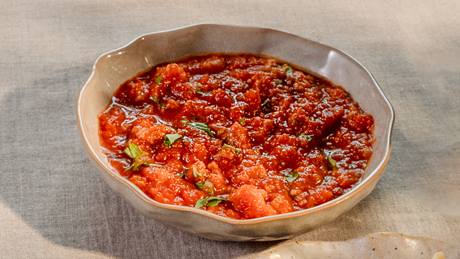 Schale mit grob pürierter Tomatensauce mit Kräutern auf hellgrauem Stoff