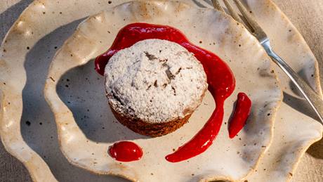 Warmes Schokoladenkuechlein mit Himbeersauce, serviert auf einem Keramikteller mit einer kleinen Gabel