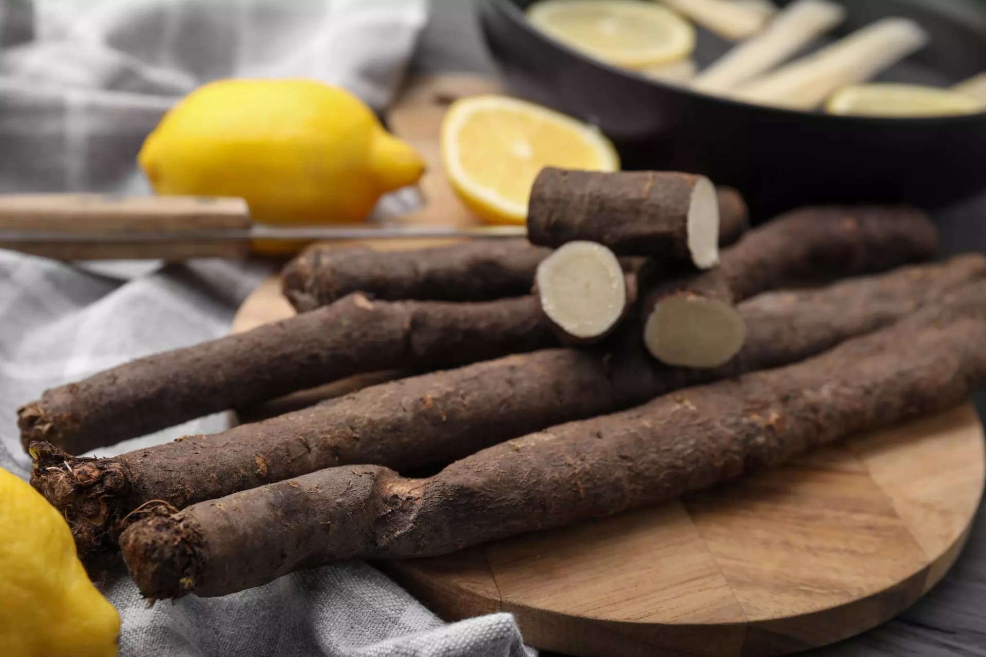 Schwarzwurzel - teilweise angeschnitten - auf einem Holzschneidebrett mit Zitronen im Hintergrund
