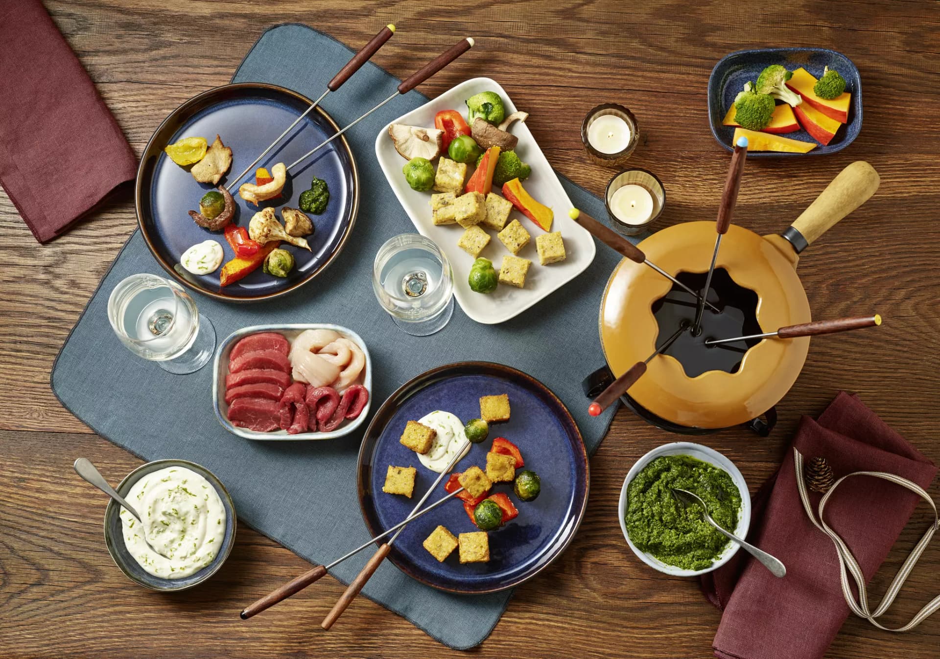 Gedeckter Fondue-Tisch mit verschiedenen Zutaten. Fleichsorten, Pesto, Gemüse und Tofu.