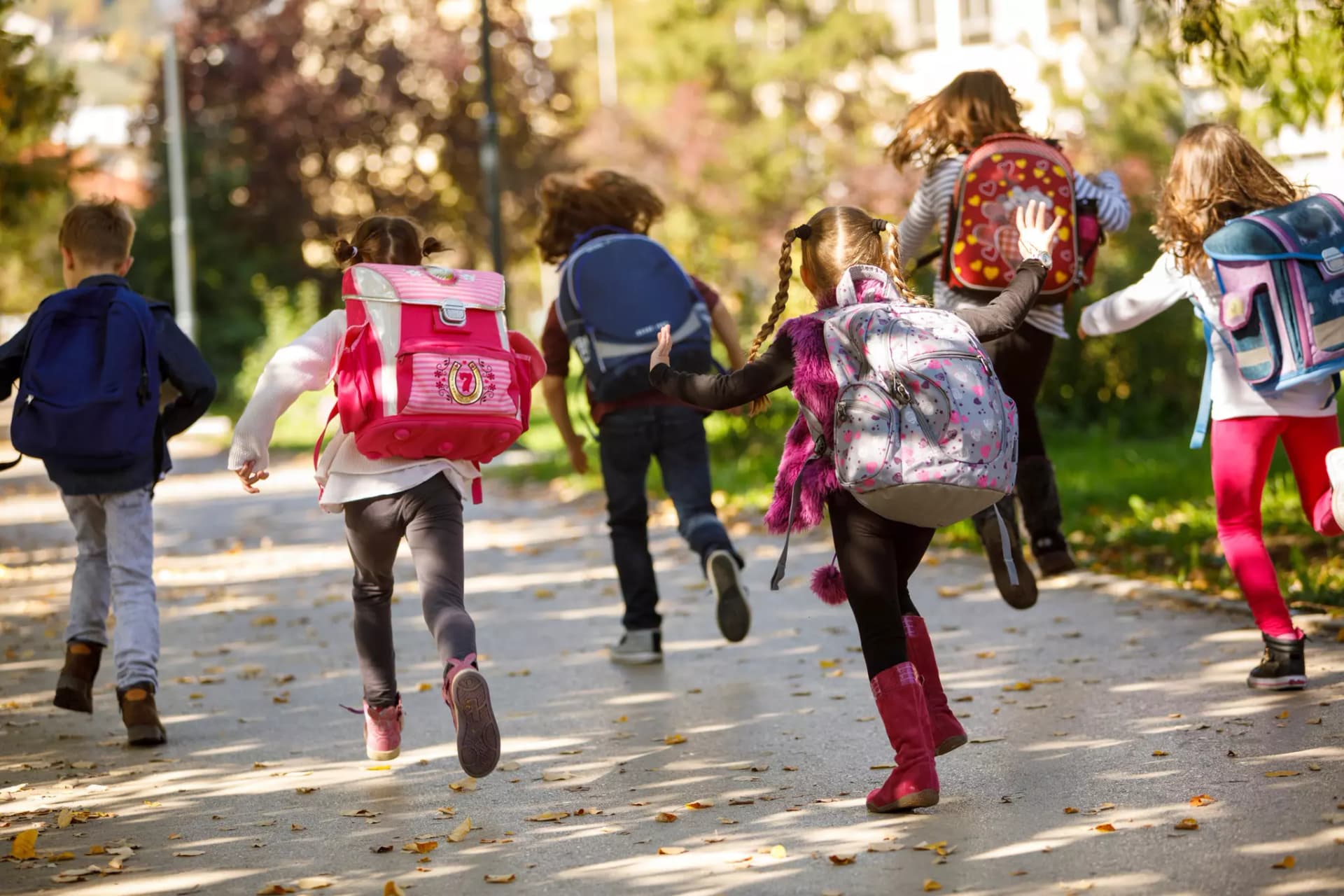 Kinder mit Schulranzen auf dem Rücken rennen von der Kamera weg über einen Hof