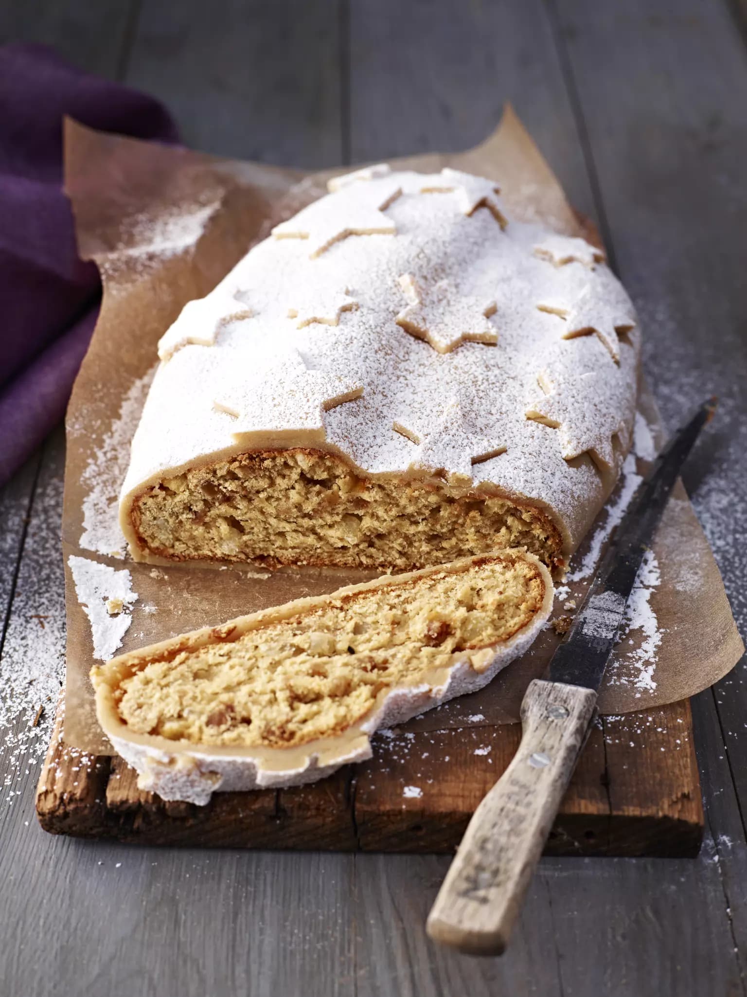 Ein Christstollen auf einem Holzbrettchen. Daneben liegt ein Messer. Der Christstollen ist außen mit Sternen deokoriert.