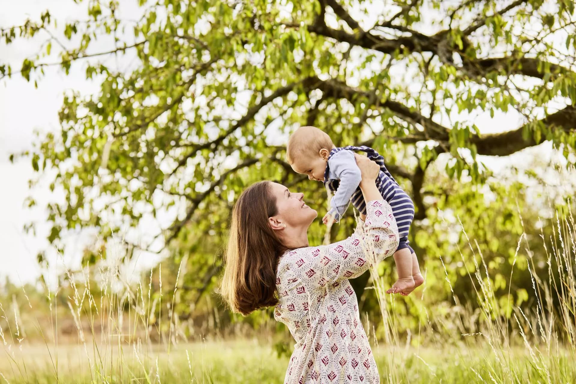 Auf einer Wiese hebt eine Mutter ihr Baby hoch