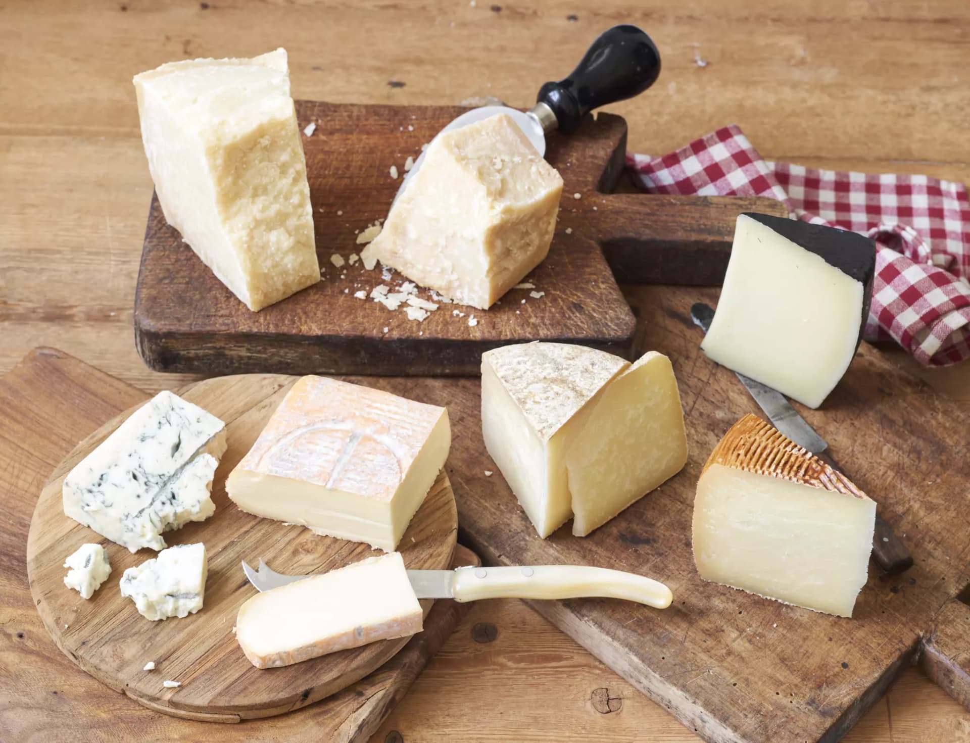Warenkunde Käse, sieben verschiedene Käsesorten auf Holzbrettern mit Käsemessern.