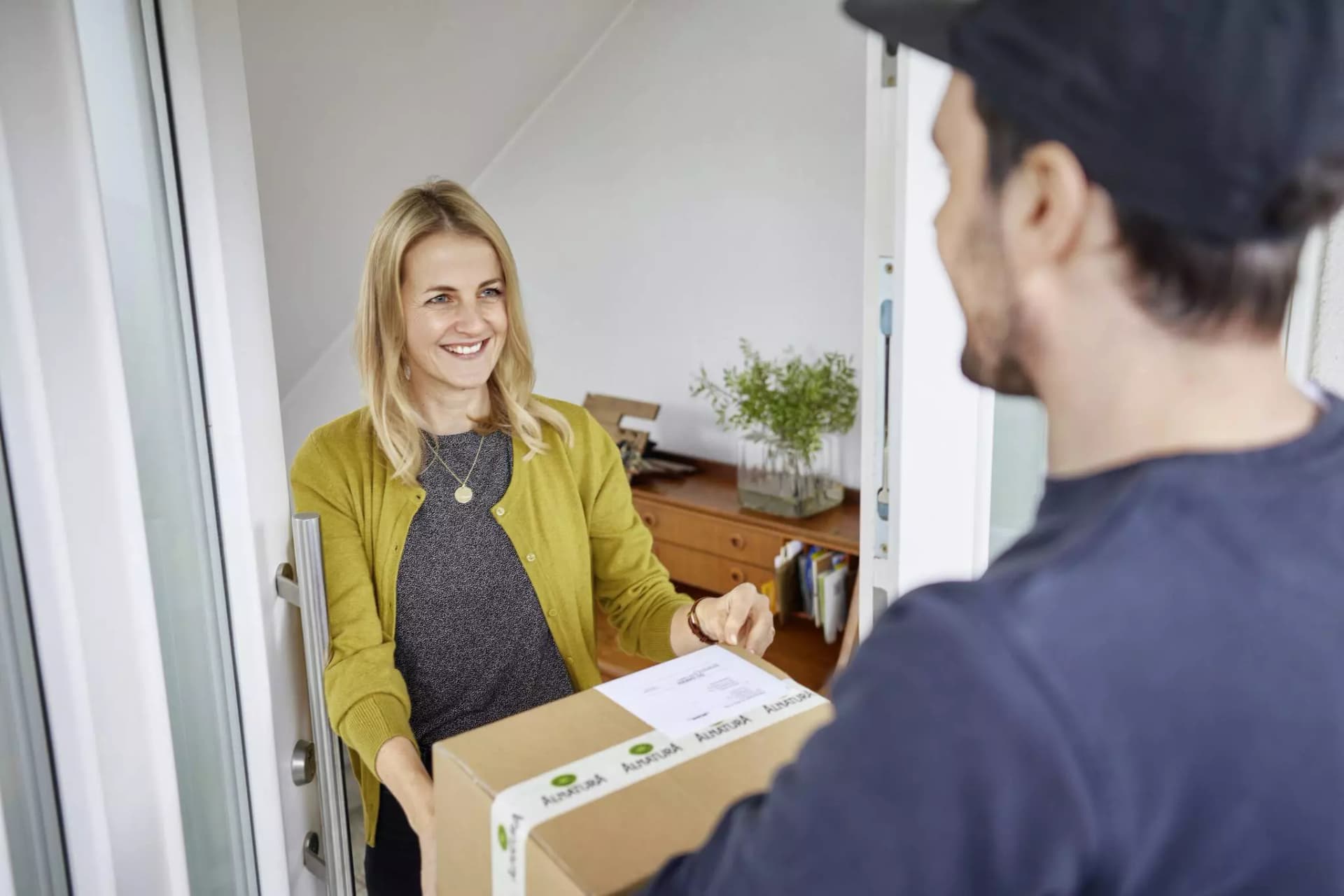 Eine Kundin nimmt an ihrer Haustür ein Paket von einem Lieferanten entgegen