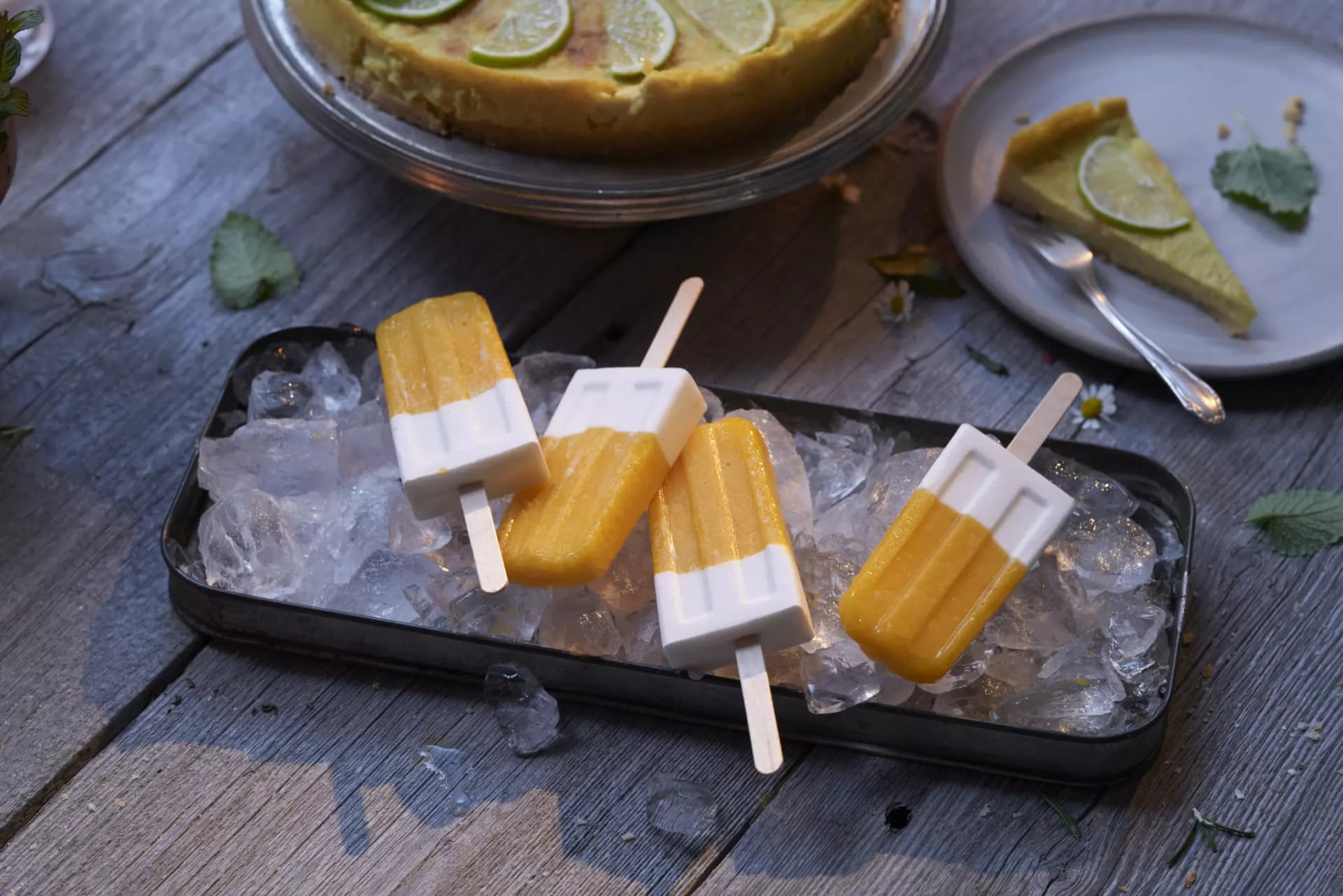 Mango-Kokos-Eis am Stiel auf einer Platte mit Eiswürfeln.