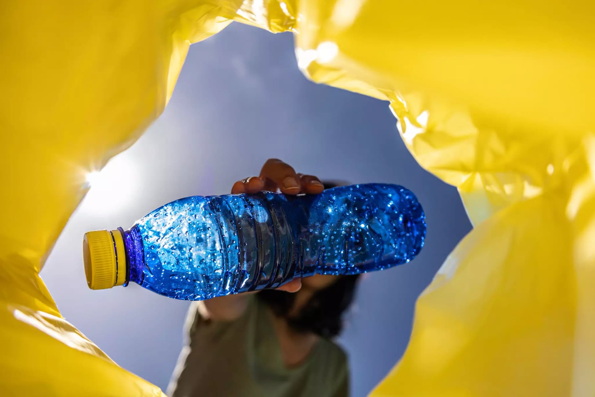 Eine blaue Plastikflasche wird in eine Gelbe Plastiktüte gesteckt