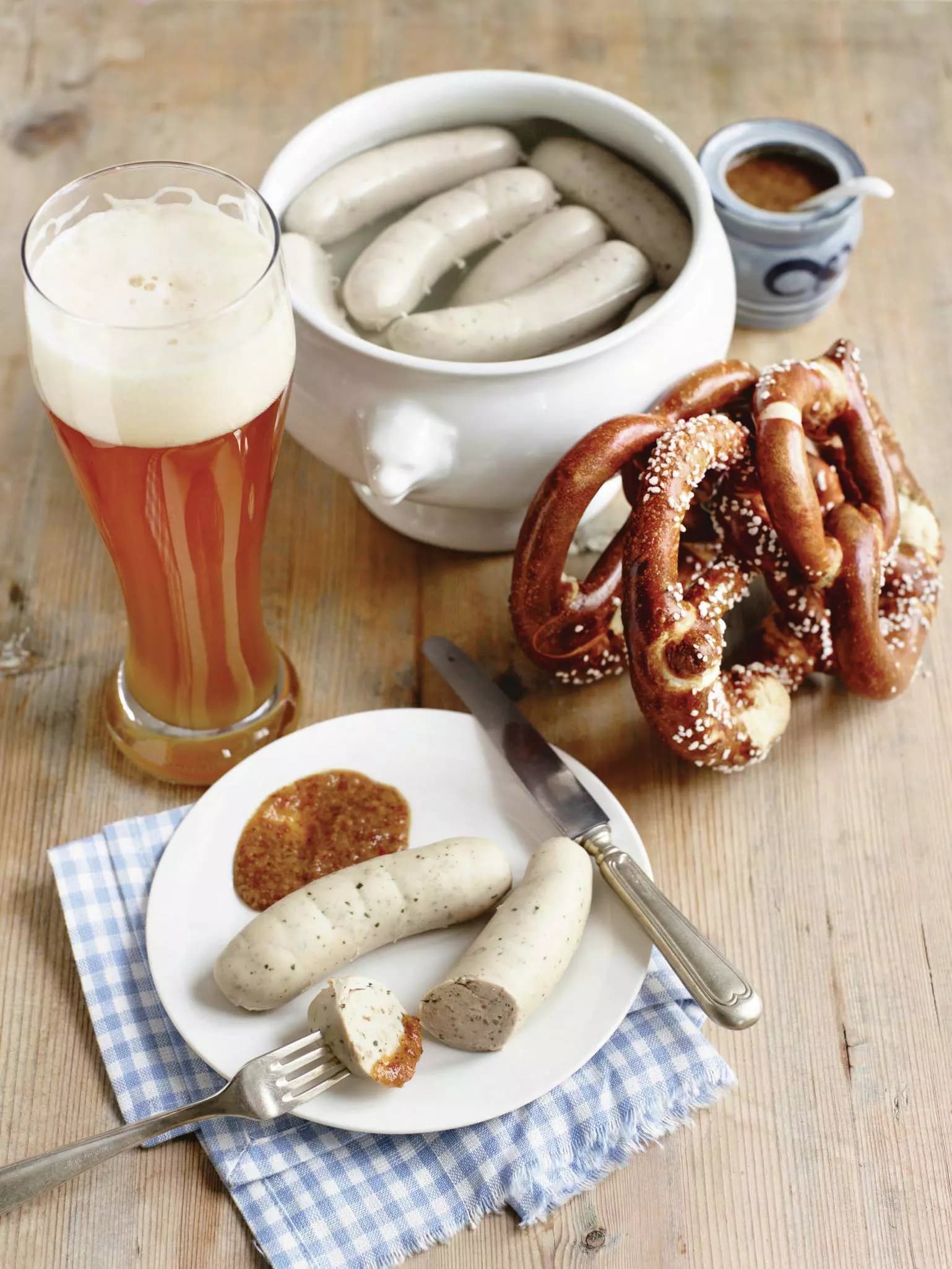 Topf mit Weißwürsten, ein Paar auf dem Teller davor mit Laugenbrezeln und ein Weißbier im Glas.