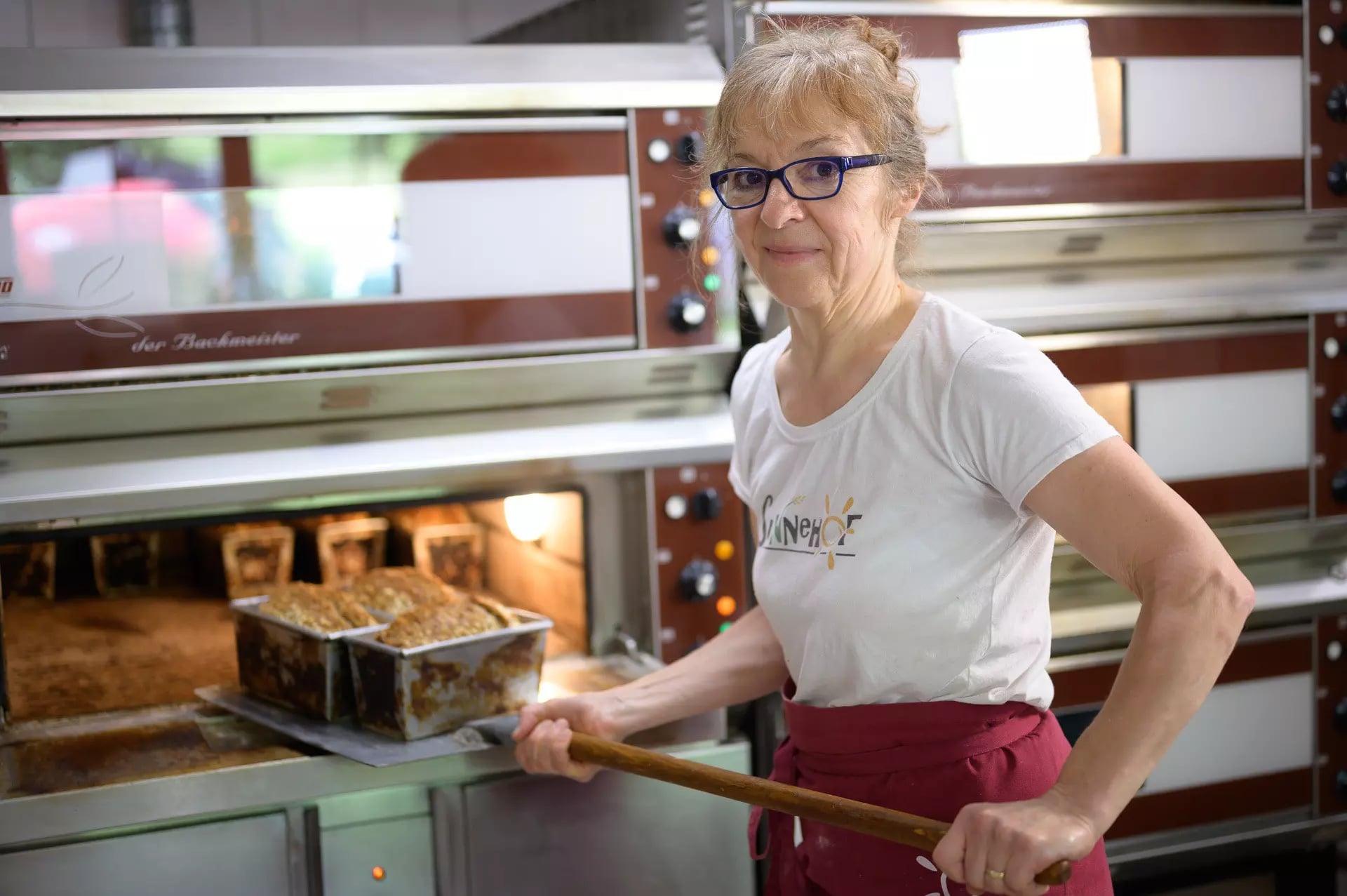 Eine Bäckerin schiebt drei Laibe Brot in der Form in den Ofen