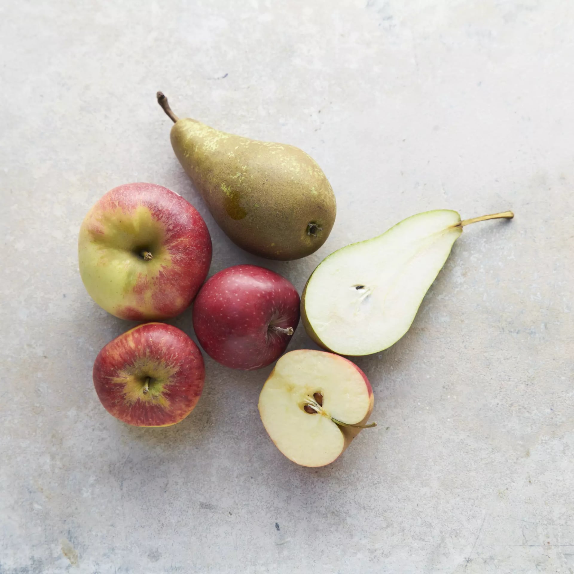 Drei Äpfel und zwei Birnen, ein halbierter Apfel und eine halbierte Birne.